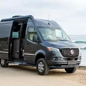 Airstream Interstate 19GT Kastenwagen am Strand mit geöffneten Türen, Meereskulisse im Hintergrund