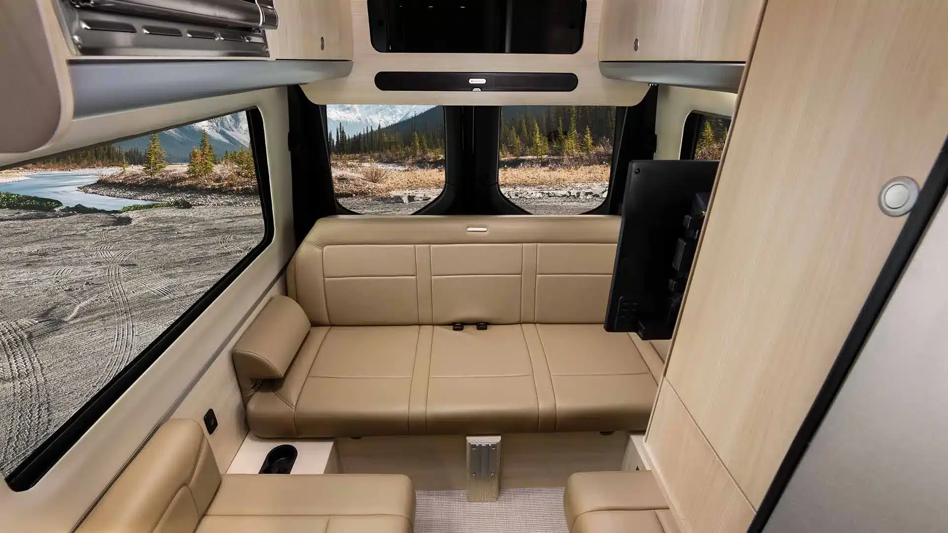 Moderner Innenraum eines Airstream Interstate 19GTX mit Sitzbereich und Blick auf die Natur durch große Fenster.