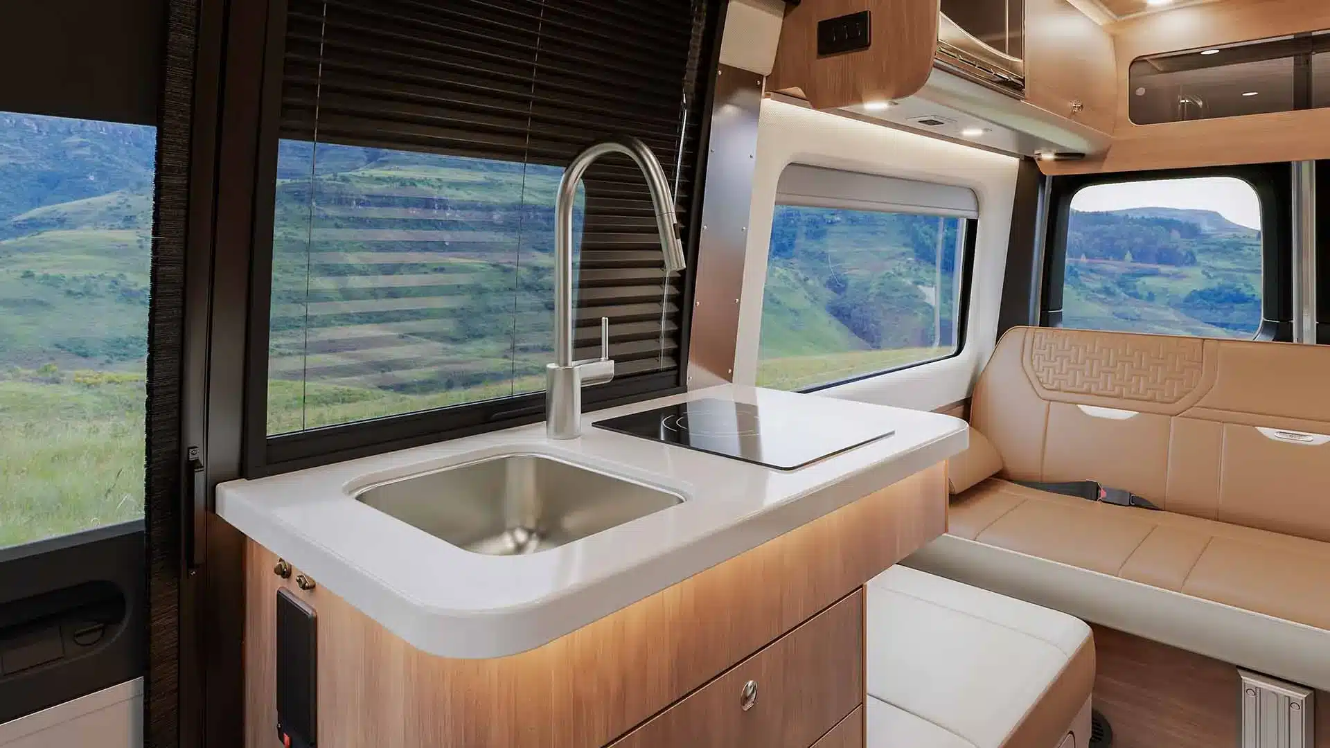 Küchenzeile und Sitzbereich im Airstream Interstate 19GTX mit Ausblick auf grüne Landschaft durch große Fenster.