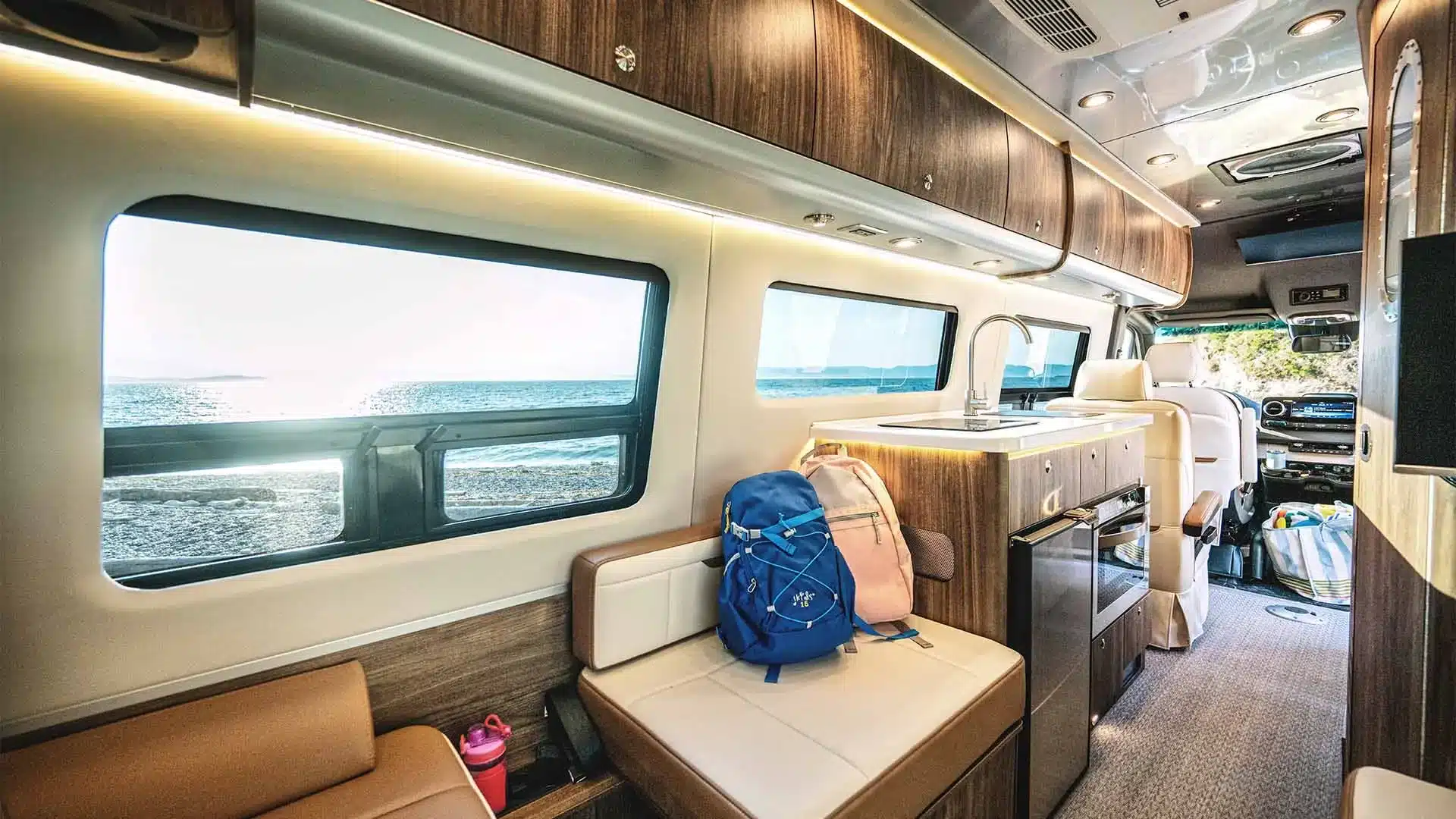 Innenraumansicht des Airstream Interstate 24GL mit eleganter Küche, Sitzbereich und Meerblick durch die großen Fenster.