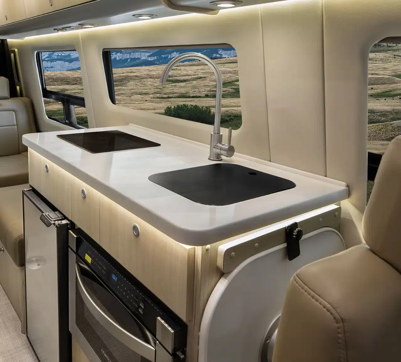 Küchenbereich mit weißer Arbeitsplatte, Induktionskochfeld, Spülbecken und Kühlschrank im Airstream Interstate 24GL Reisevan.