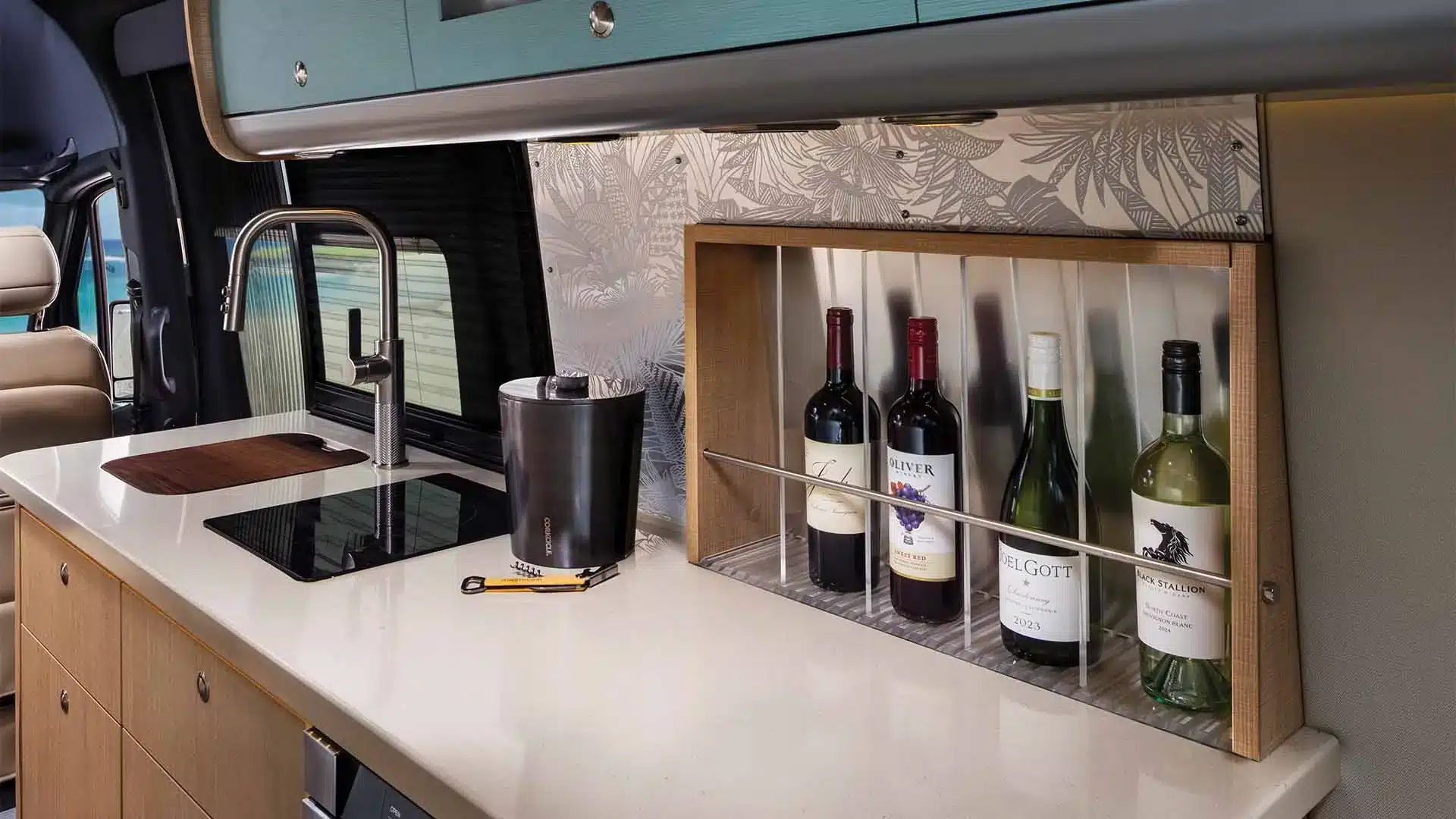 Innenansicht der modernen Küche im Airstream Interstate 24GT Van mit Mineralwerkstoff-Arbeitsfläche, Spüle, Kochfeld und integrierter Weinablage.