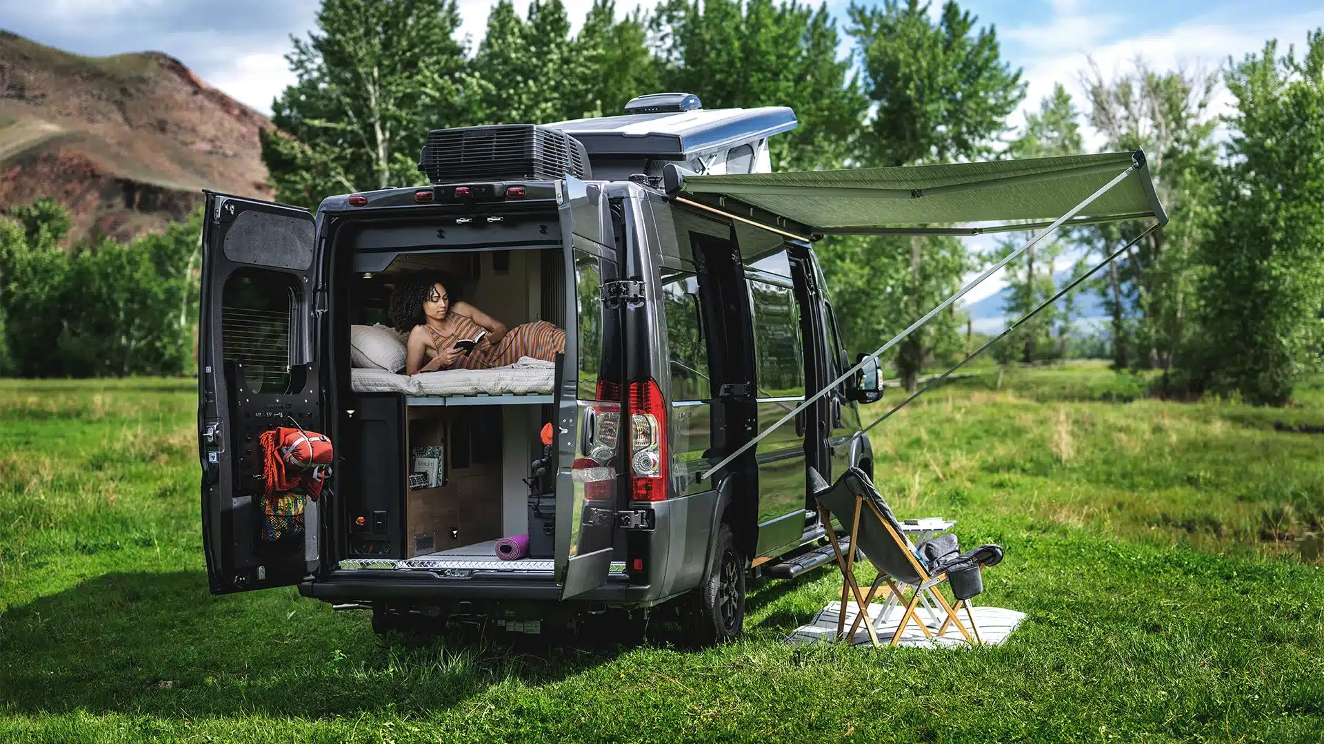 Airstream Rangeline 2026 Campervan mit Outdoor-Setup und geöffneter Heckklappe auf einer grünen Wiese.