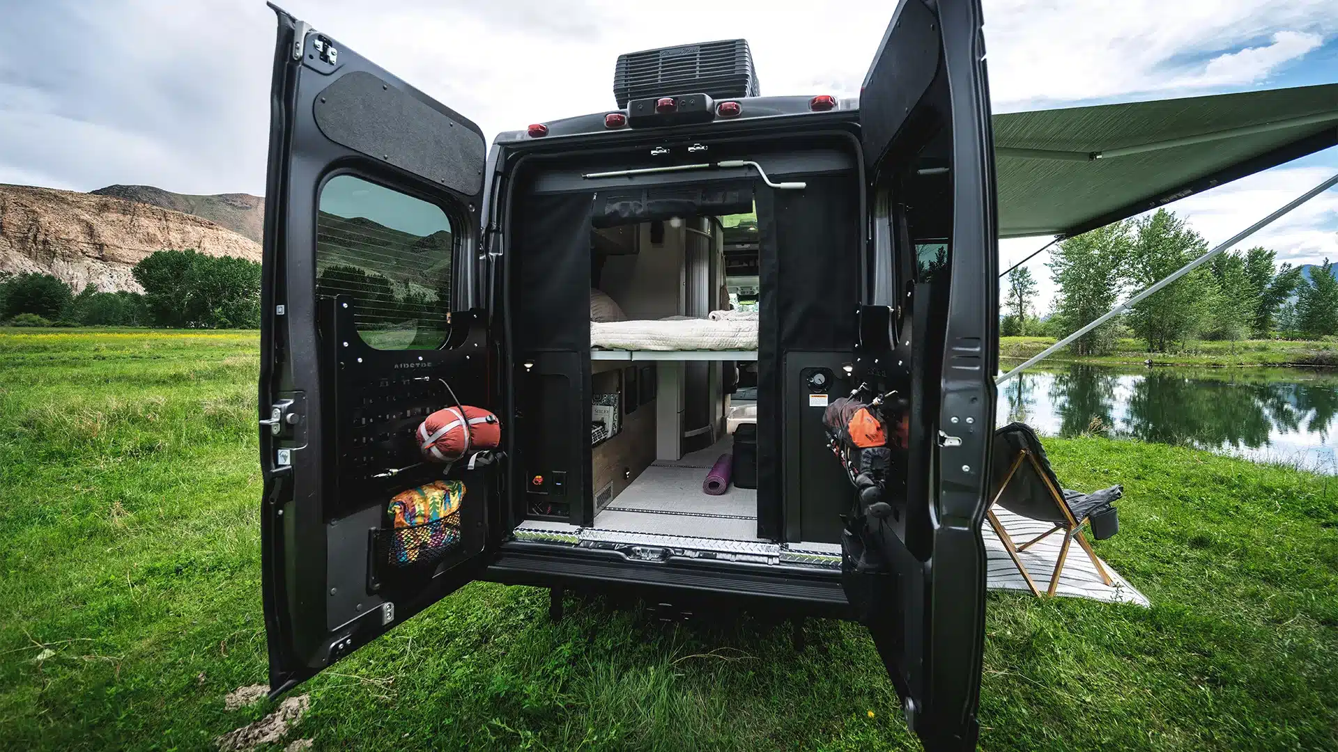 Der Airstream Rangeline 2026 mit geöffneten Hecktüren, sichtbarem Stauraum, Liegefläche und Outdoor-Setup neben einem See.