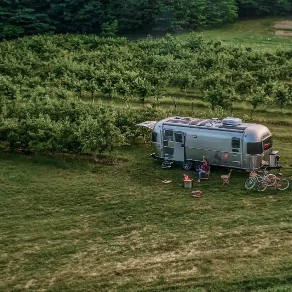 Airstream Trade Wind 2026 Reiseanhänger mit Pickup auf einer grünen Wiese, umgeben von Obstbäumen.