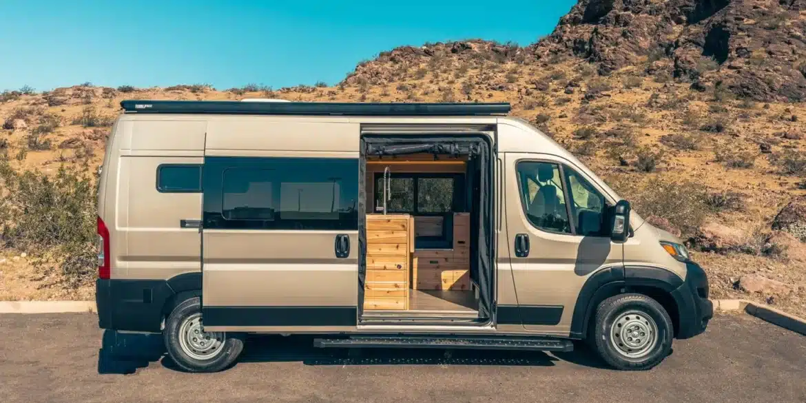 RAM Promaster 2500 High Roof 159 mit geöffnetem Seiteneinstieg, Blick auf maßgefertigten Innenausbau aus Holz in karger Wüstenlandschaft