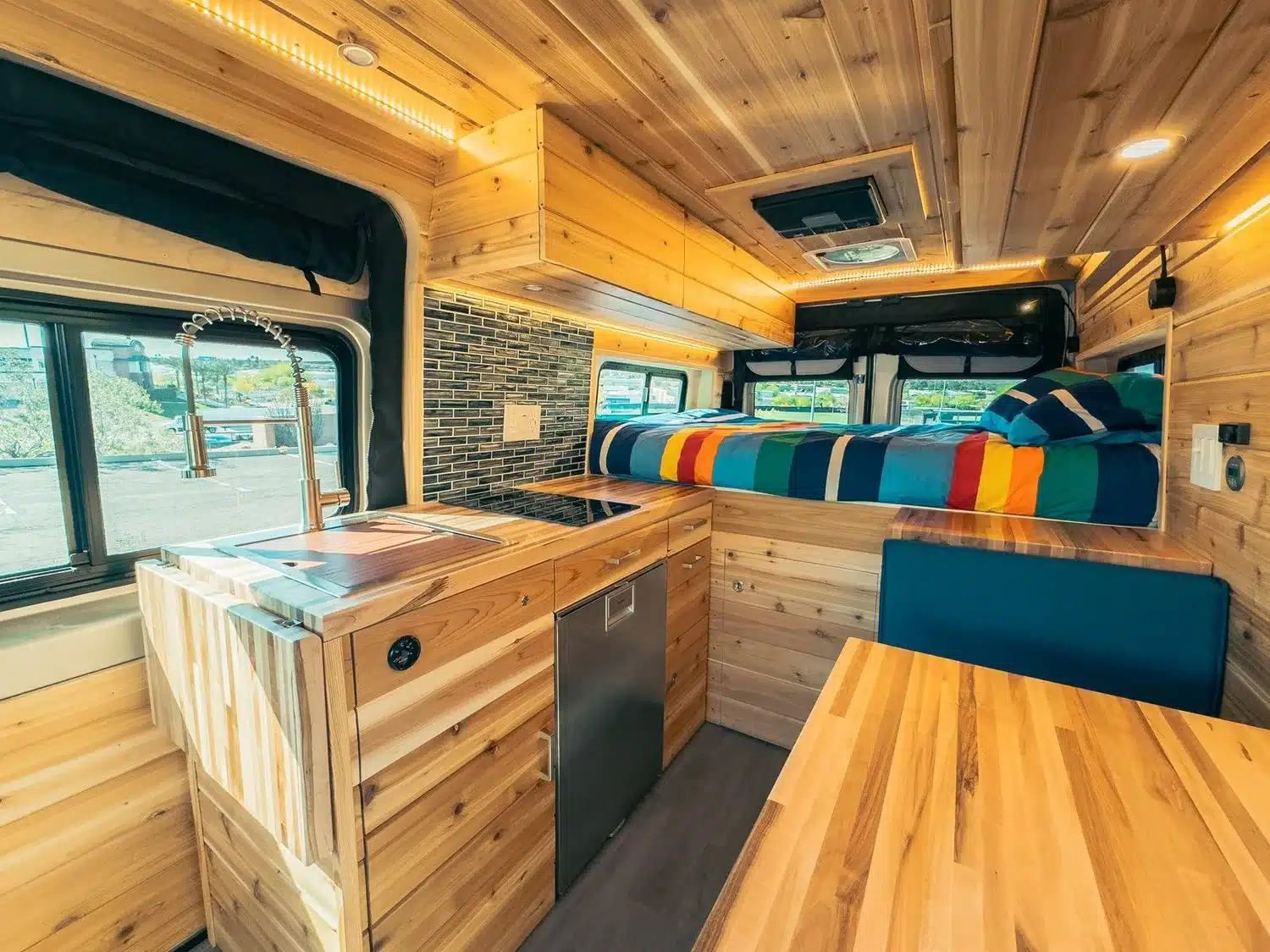 Innenraum eines AQUAVAN Campervans auf RAM Promaster 2500 High Roof 159 mit Holzverkleidung, Küche, Essbereich und Querbett.