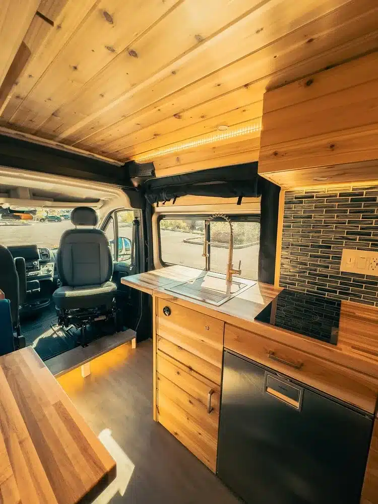 Hochwertiger Innenausbau eines Camper-Vans mit Holzverkleidung, moderner Küchenzeile, Induktionskochfeld, Spüle und Dometic-Kühlschrank