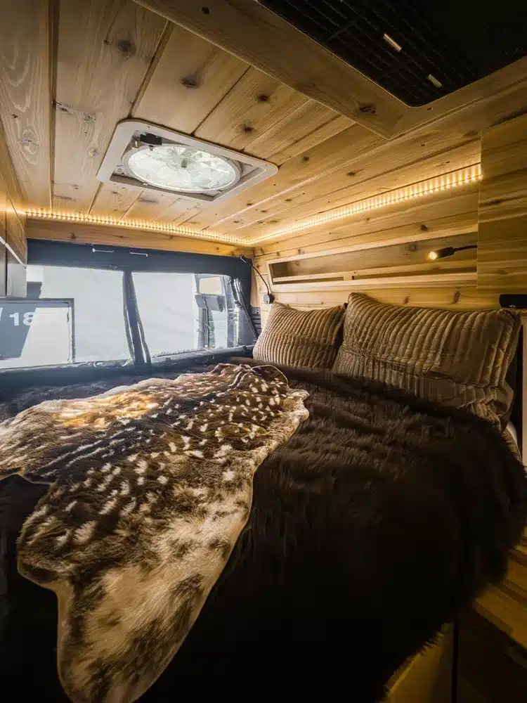 Innenraum des Boho Jean Campervans mit gemütlichem Doppelbett, Holzverkleidung und Oberlicht.