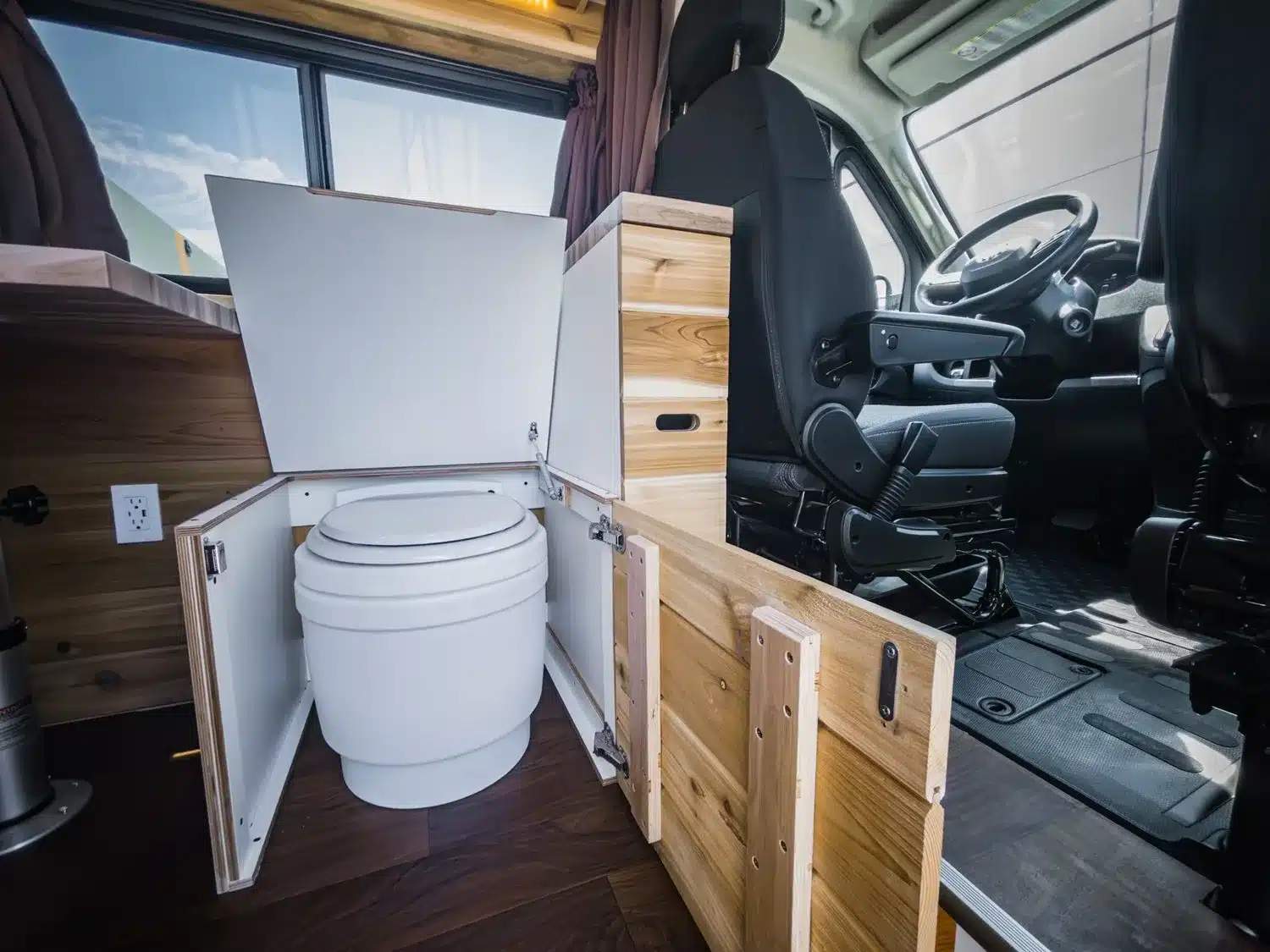 Laveo-Dryflush-Toilette in einem ausgebauten Kastenwagen-Boho Jean mit geöffnetem Holzschrank.
