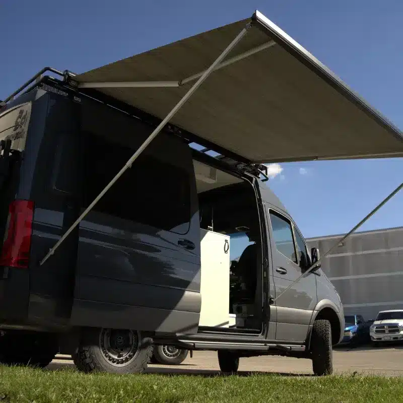 Campervan Bruce Peninsula von Vancini Conversions seitlich mit ausgefahrener Markise, offene Schiebetür und Blick auf das hell gestaltete Küchenmodul.
