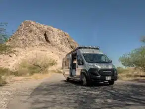 Butterfly RAM Promaster EXT Camper Van geparkt vor einer felsigen Bergkulisse unter blauem Himmel.