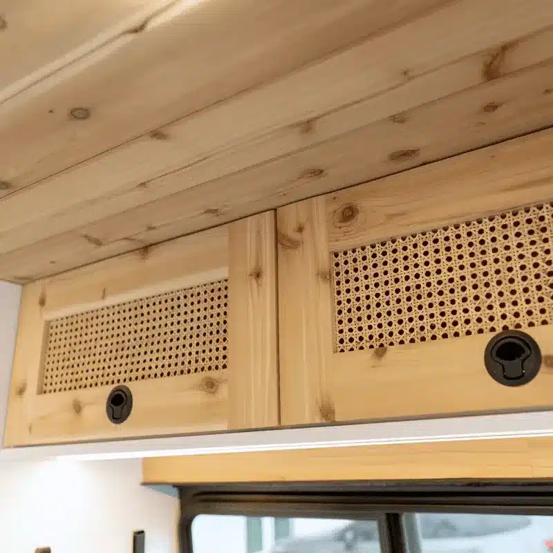 Holzstaufach mit Geflecht und schwarzen Griffen im Innenraum eines Campervans