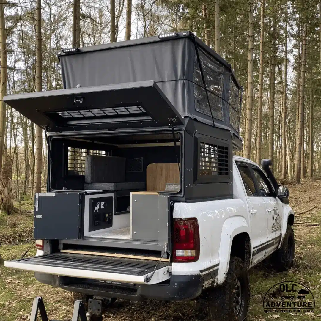 Capra Camper 3.0 Pop-up-Wohnkabine montiert auf einem weißen Doppelkabiner-Pick-up mit geöffnetem Heck im Wald