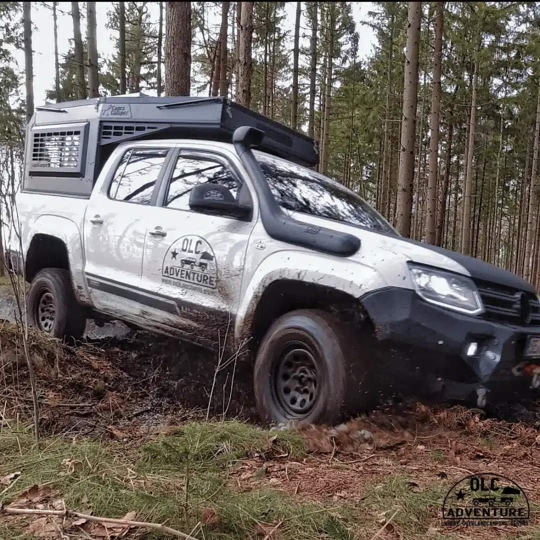 Pick-up mit Capra Camper 3.0 Wohnkabine von OLC Adventure fährt durch matschigen Waldweg