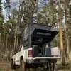 Capra Camper 3.0 Wohnkabine montiert auf Pick-up, aufgeklappt im Wald, Heckklappe geöffnet, Ausstattung sichtbar