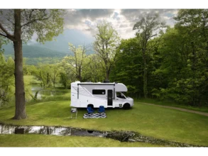 Chateau Sprinter 24LT Wohnmobil auf Sprinter-Basis, geparkt auf einer Wiese am Waldrand, mit Campingstühlen vor dem Fahrzeug.