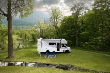 Chateau Sprinter 24LT Wohnmobil auf Sprinter-Basis, geparkt auf einer Wiese am Waldrand, mit Campingstühlen vor dem Fahrzeug.