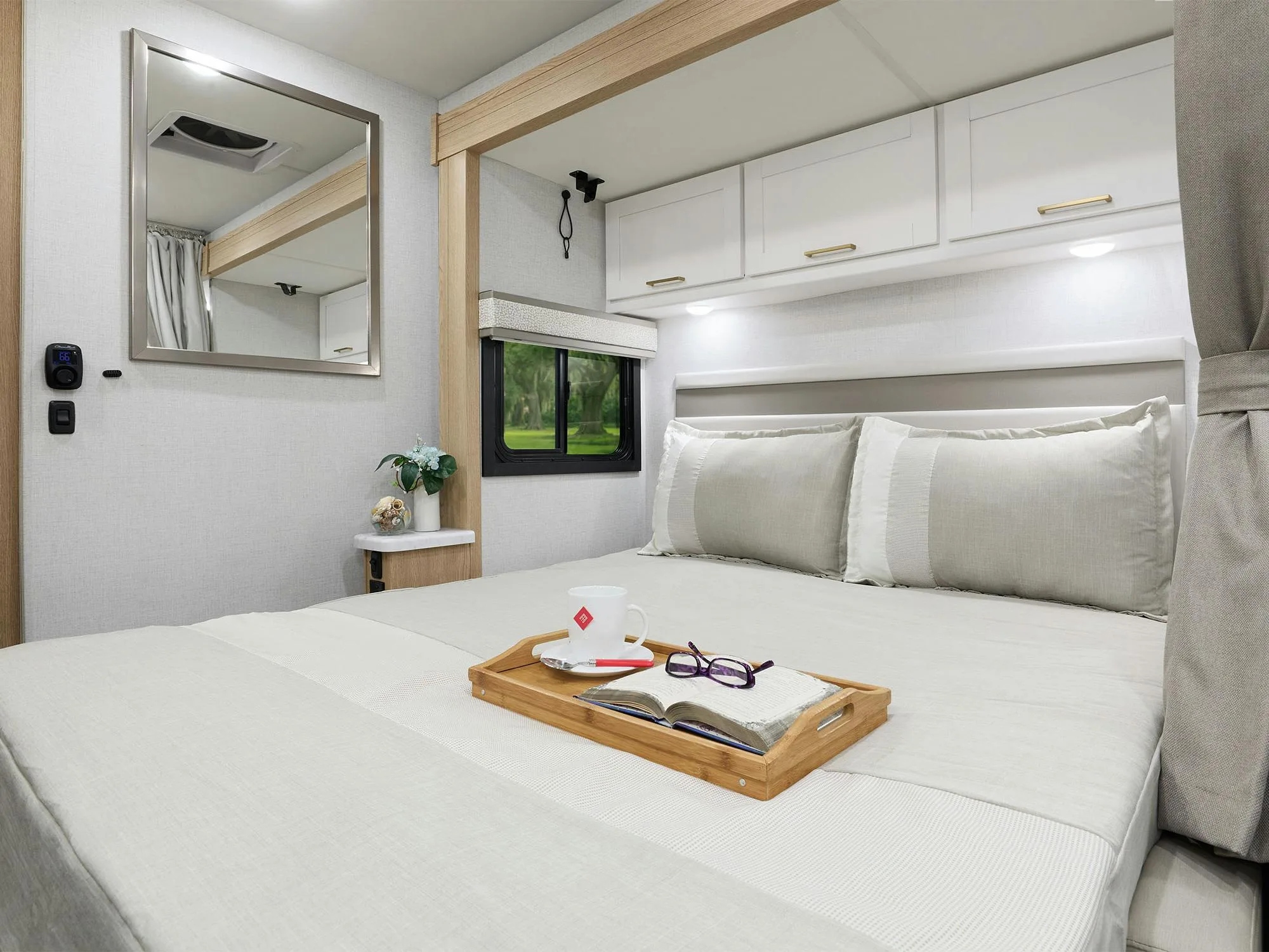 Wohnbereich mit ausgeklapptem Murphy-Bett im Chateau Sprinter 24LT, Tablett mit Buch und Tasse auf dem Bett.