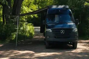 Der Copper Falls Campervan von VanCini Conversions steht mit ausgefahrener Markise im Grünen auf einem Waldweg.