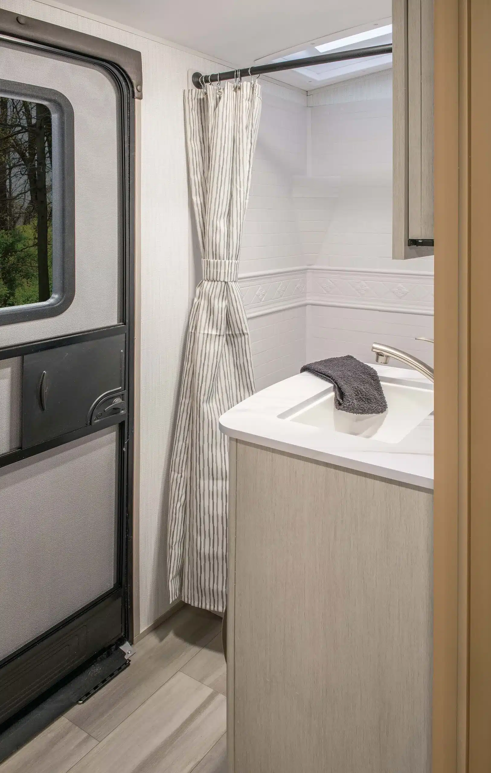 Blick ins Badezimmer des Cruiser Embrace EL26RB mit Waschbecken, Duschvorhang und Tür.