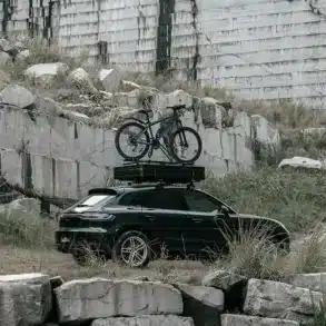 Auto mit geschlossenem Summit Explorer 140 Hartschalen-Dachzelt und Fahrrad auf dem Dach vor Steinwand
