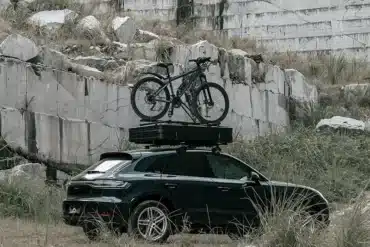 Auto mit geschlossenem Summit Explorer 140 Hartschalen-Dachzelt und Fahrrad auf dem Dach vor Steinwand