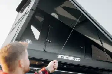 Person baut das Dark Barracks Grand Hardside-Dachzelt auf einem Fahrzeug auf.