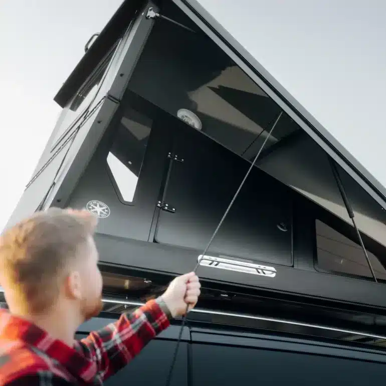 Person baut das Dark Barracks Grand Hardside-Dachzelt auf einem Fahrzeug auf.