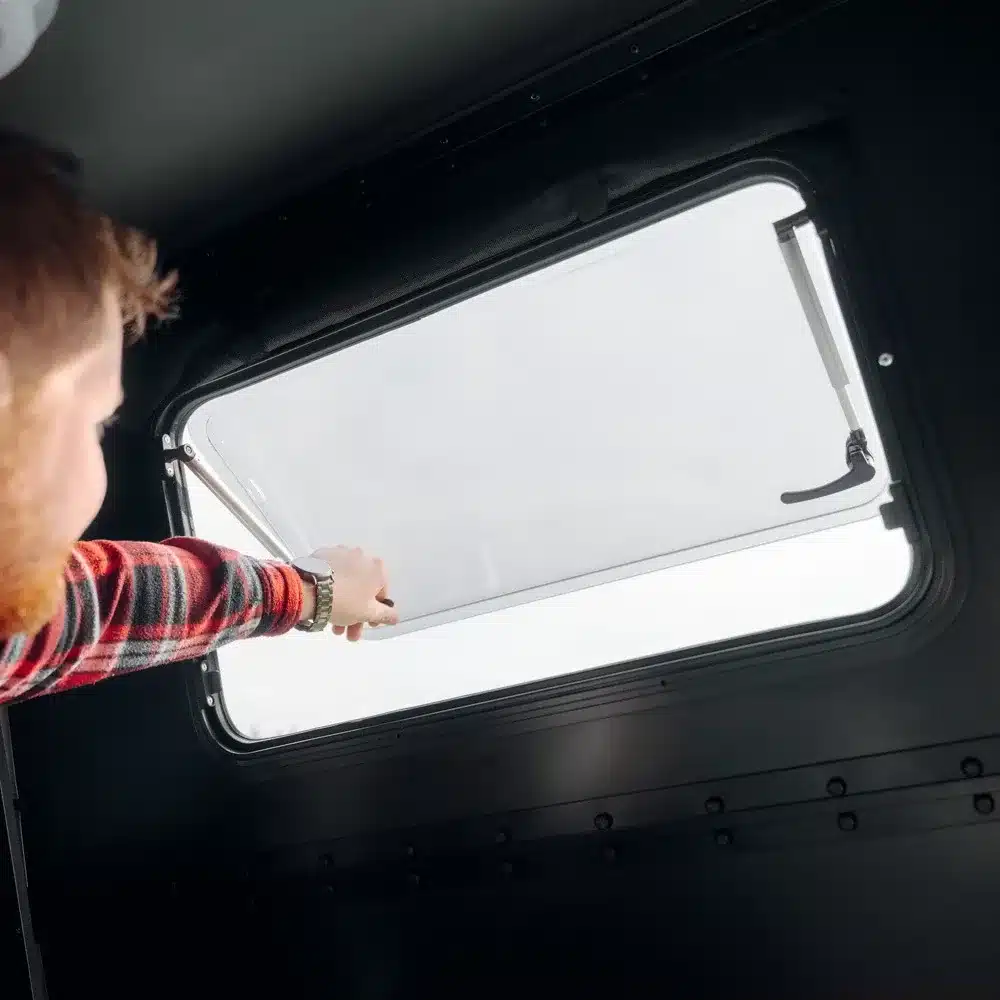 Person öffnet das Fenster im Inneren eines Hardside-Dachzelts Dark Barracks Grand.