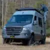 Dark MODE XO Campervan auf Mercedes Sprinter-Basis im Gelände mit Person auf der Dachleiter.