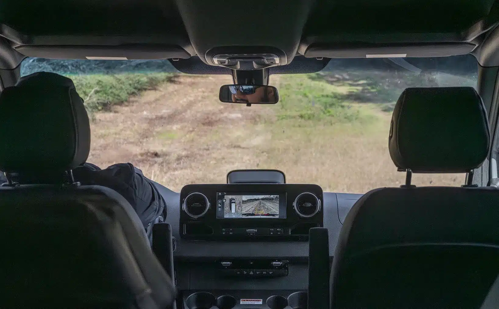Innenraum eines Mercedes-Benz Sprinter Dark MODE XO mit digitaler Rückfahrkamera und Blick hinaus auf einen unbefestigten Weg