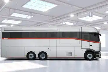 Seitenansicht des Dembell Side Storage Luxusreisemobils mit glatter Außenhaut und roten Zierstreifen, stehend in einer hellen Halle.