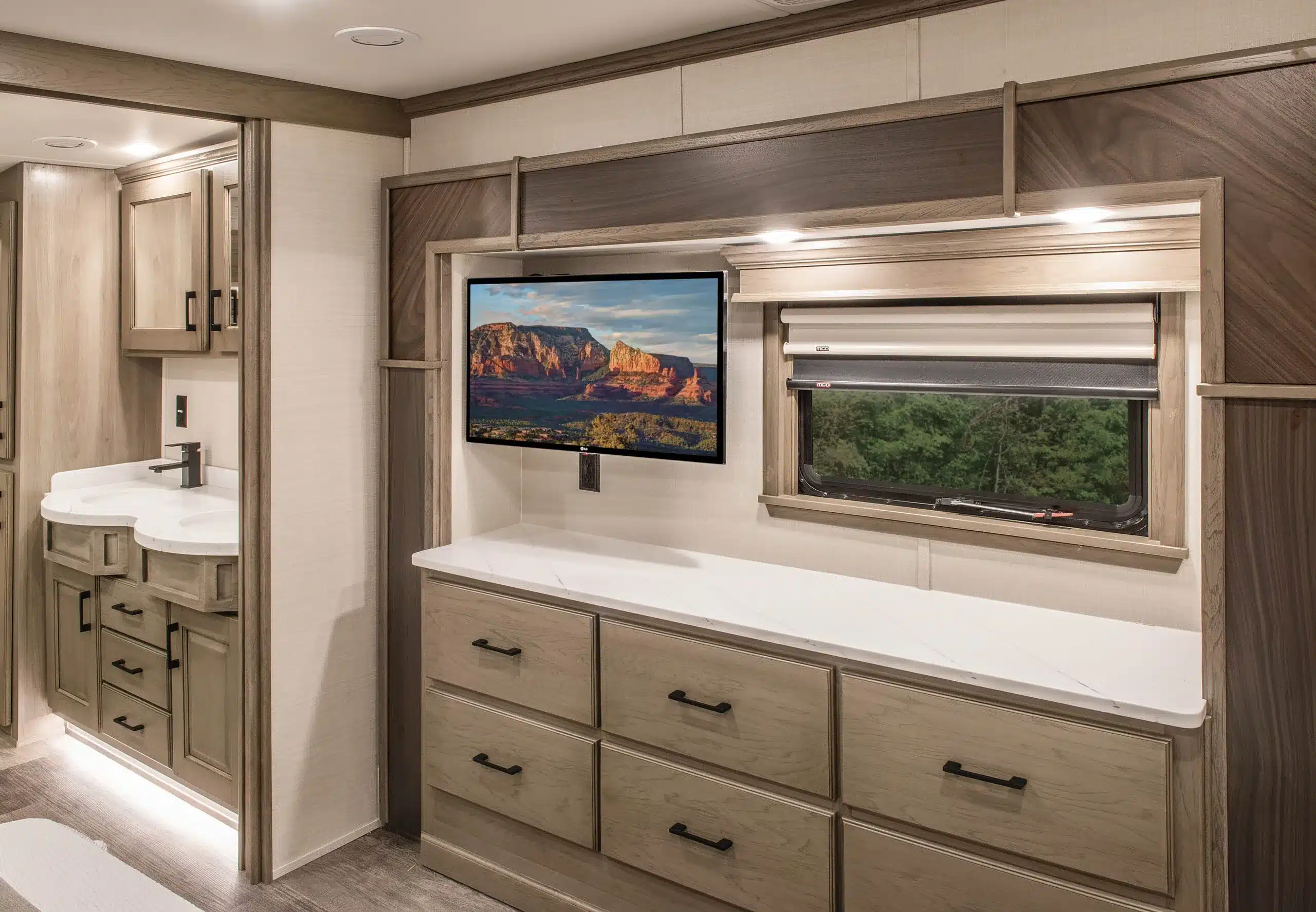 Modern eingerichteter Innenraum eines DRV MS Houston Fifth Wheel Wohnwagens mit TV, Kommode, Fenster und Badezimmer