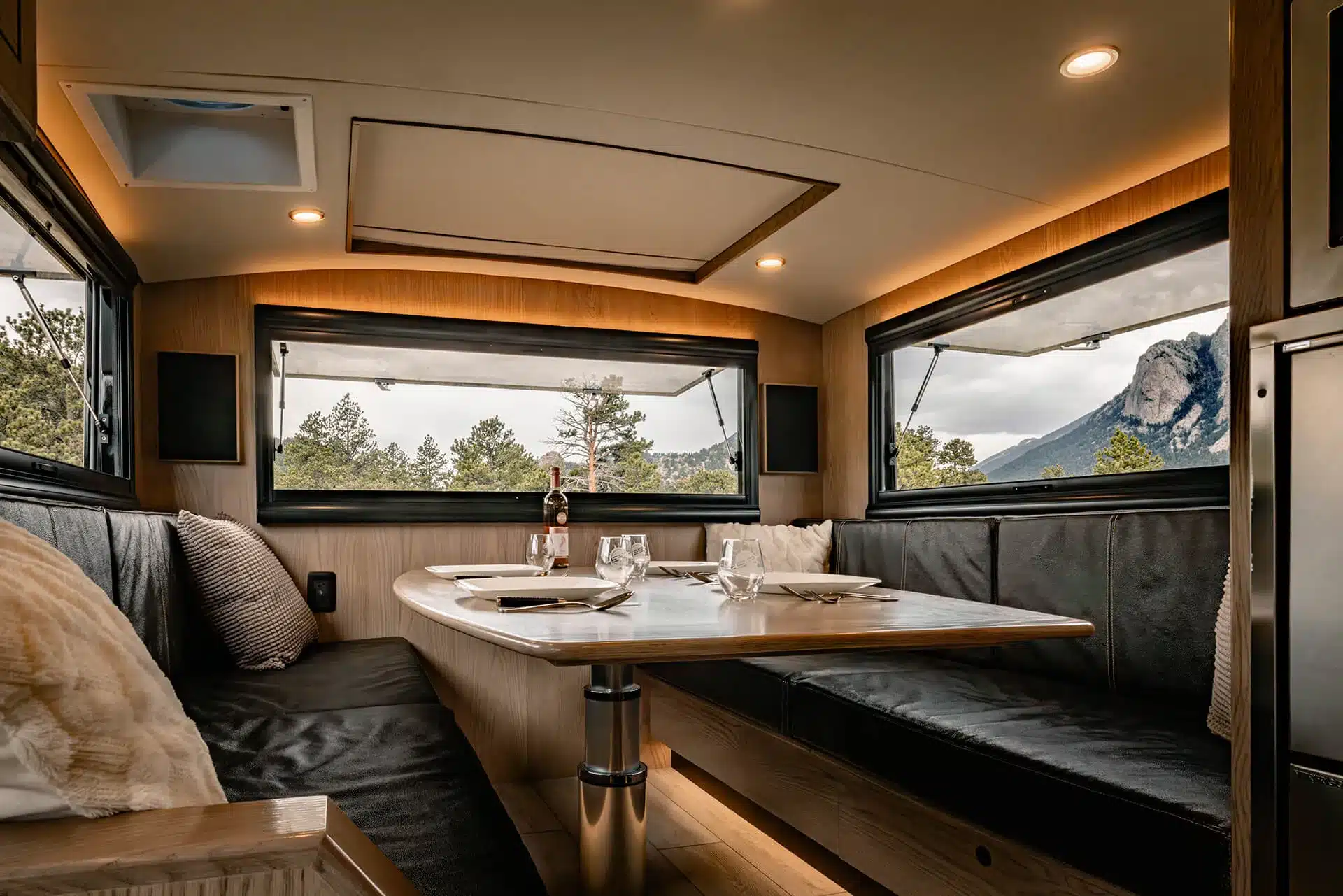 Gemütliche Sitzecke und Esstisch im Innenraum des EarthRoamer SX Explore, umgeben von großen Fenstern mit Blick auf Berge und Natur.