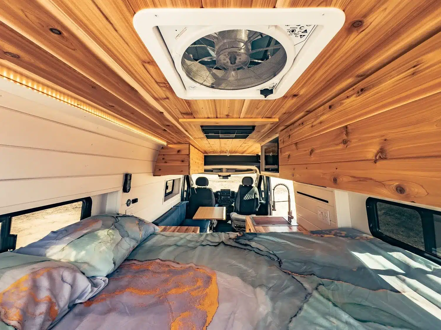Blick in den Innenraum eines Faith RAM Promaster Camper Vans mit Holzdecke, großem Bett im Vordergrund und einem MaxxAir Dachventilator