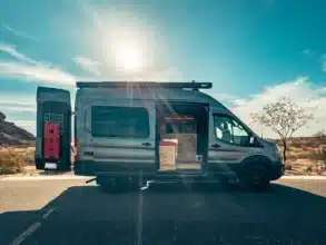 Ford Transit Trail Camper Van mit geöffnetem Heck und Blick auf den Innenausbau in sonniger Landschaft
