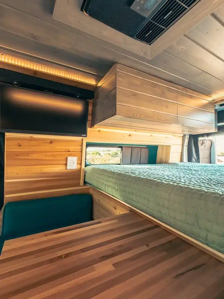 Wohnbereich eines Ford Transit Trail 350 Camperausbaus mit massivem Holztisch, Face-to-Face-Sitzgruppe, großem Bett, LED-Ambientebeleuchtung und Stauraum