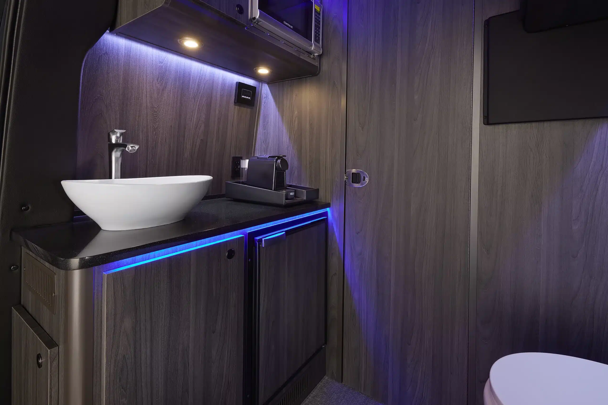 Innenansicht der Küchenzeile und des Badezimmers im Grech LUSSO Lounge mit Waschbecken, Kühlschrank, Nespresso-Maschine und Toilette