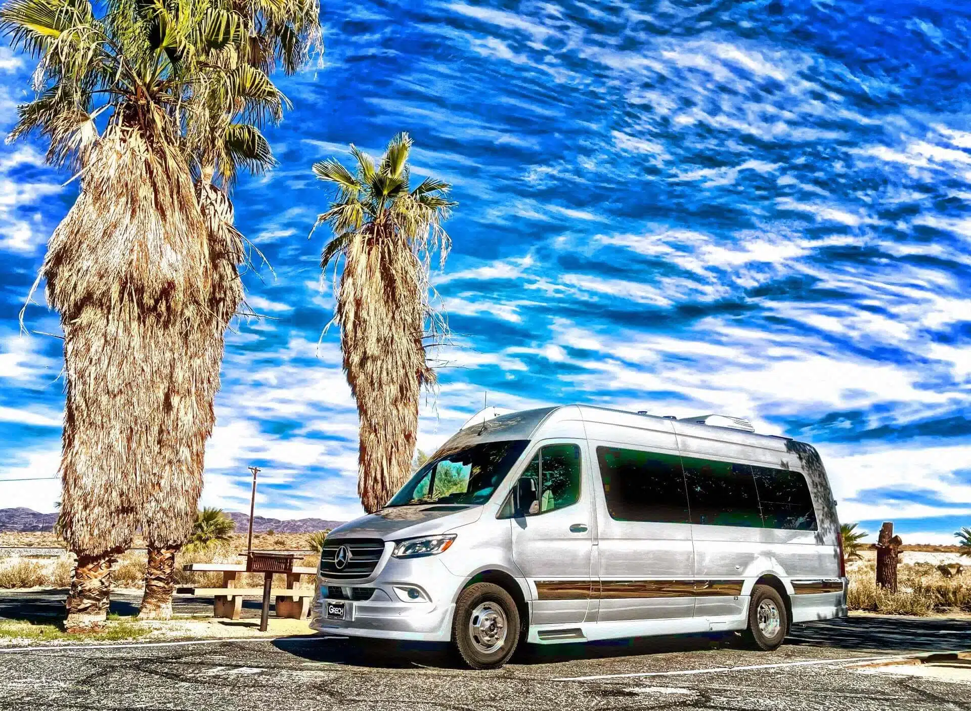 Grech RV STRADA-ion AWD Campervan auf Mercedes Sprinter Basis in silber, geparkt vor Palmen unter blauem Himmel in der Wüste.