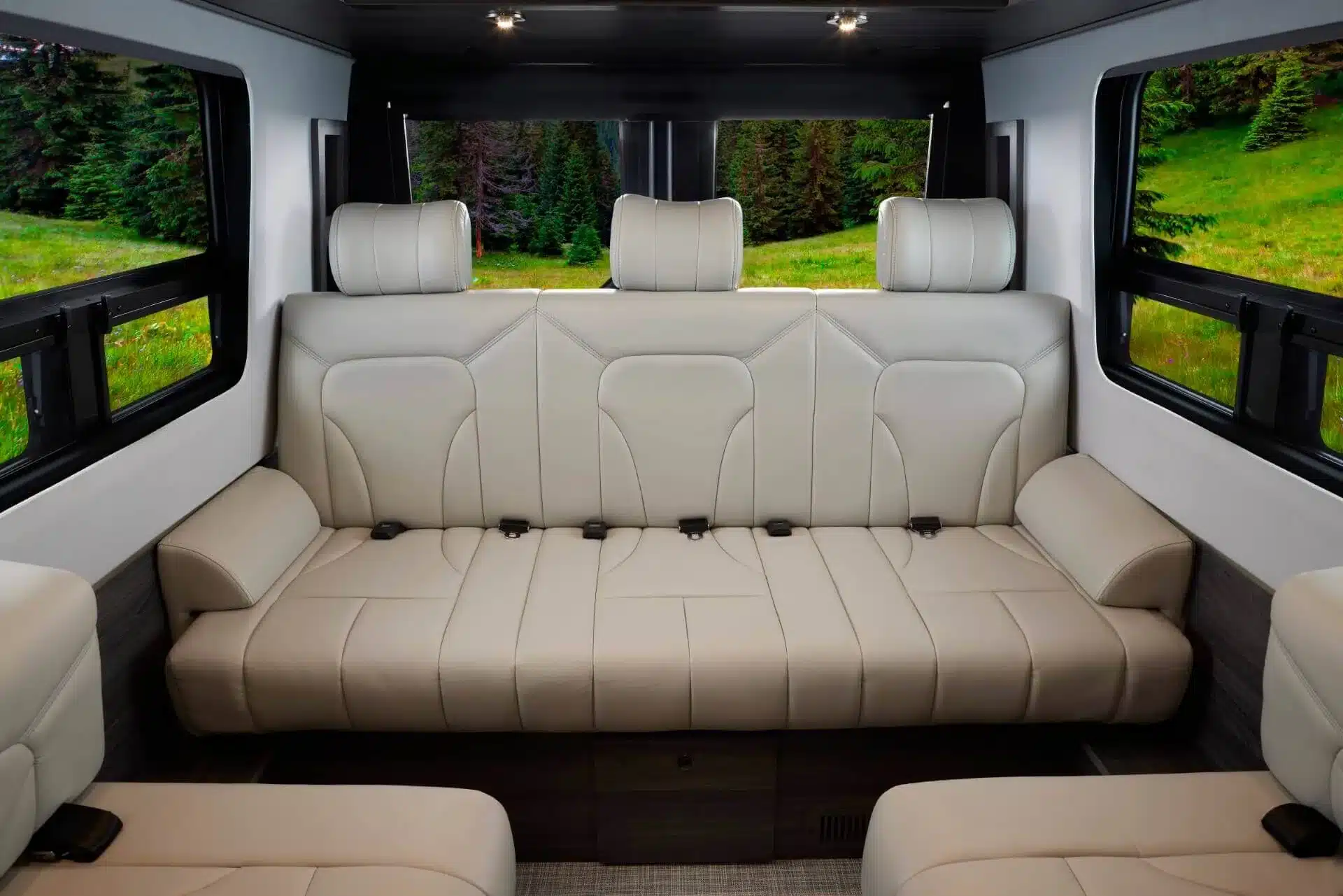 Luxuriöse beige Sitzbank mit Kopfstützen im Innenraum eines Grech RV STRADA-ion AWD Campervans auf Mercedes Sprinter Basis, mit großen Fenstern und Blick ins Grüne.