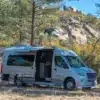 2026 Grech RV Strada-ion Campervan mit Markise und Stühlen beim Camping in einer felsigen Waldlandschaft