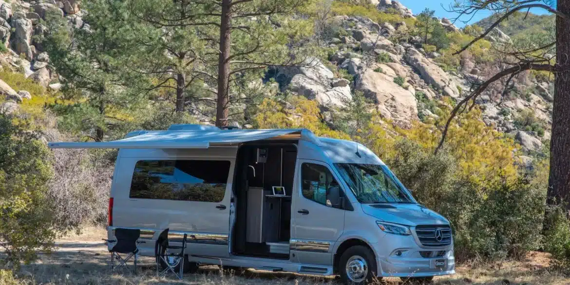 2026 Grech RV Strada-ion Campervan mit Markise und Stühlen beim Camping in einer felsigen Waldlandschaft
