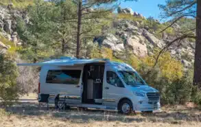 2026 Grech RV Strada-ion Campervan mit Markise und Stühlen beim Camping in einer felsigen Waldlandschaft