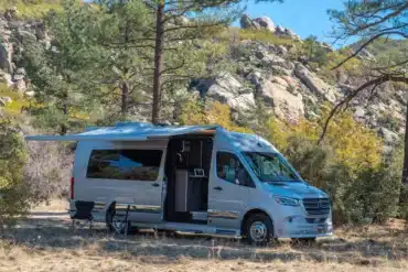 2026 Grech RV Strada-ion Campervan mit Markise und Stühlen beim Camping in einer felsigen Waldlandschaft