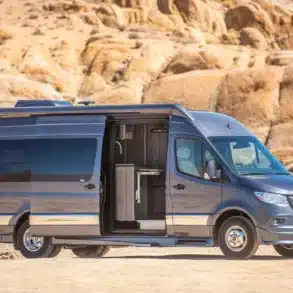 Grech Terreno-ion AWD Kastenwagen auf Mercedes-Benz Sprinter-Basis in der Wüste, seitliche Aussicht mit geöffneter Schiebetür.