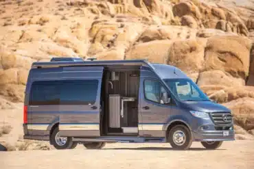 Grech Terreno-ion AWD Kastenwagen auf Mercedes-Benz Sprinter-Basis in der Wüste, seitliche Aussicht mit geöffneter Schiebetür.