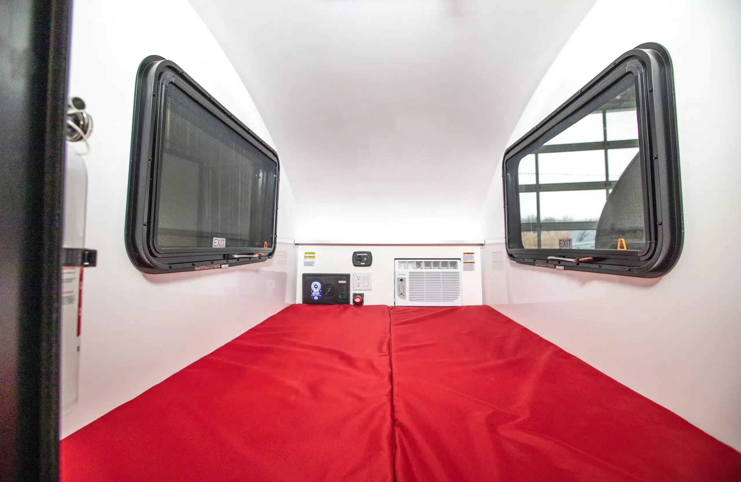 Innenansicht des Helio HE-3S Mikro-Wohnwagens mit rotem Doppelbett und zwei Fenstern