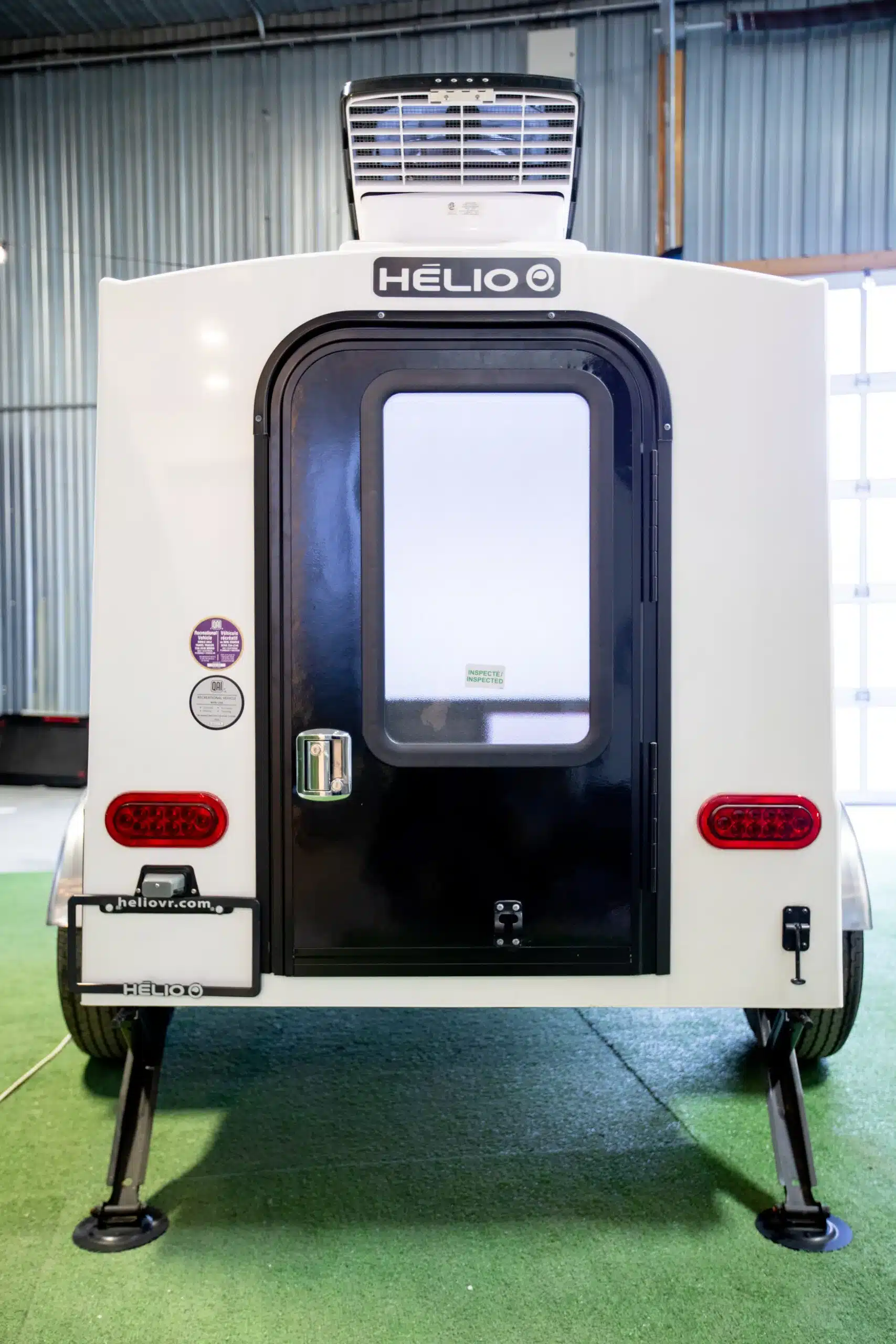 Rückseite des Helio HE-3S Mikro-Wohnwagens mit Tür, Rücklichtern und Klimaanlage in einer Halle