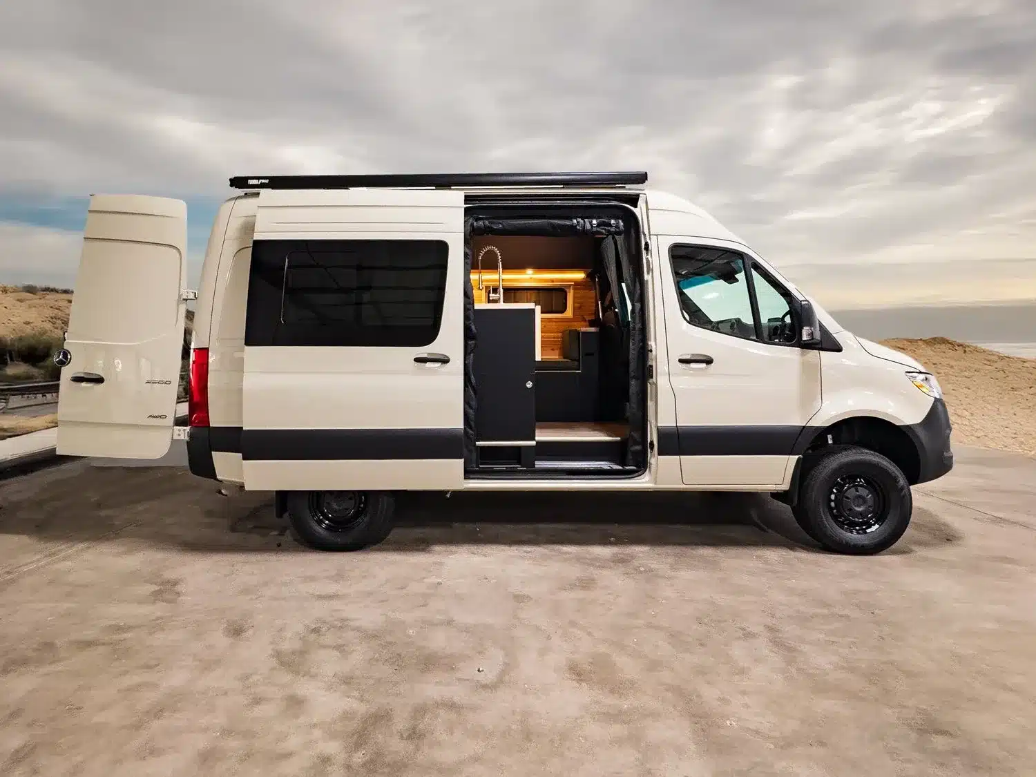 Individuell ausgebauter Hive Hideaway Campervan auf Basis eines Mercedes-Benz Sprinter 144” High Roof mit offener Schiebetür, sichtbar ist der Innenausbau mit Sitzgruppe und Stauraum.